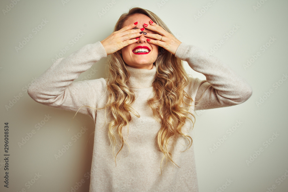 Beautiful woman wearing winter turtleneck sweater over isolated white background covering eyes with hands smiling cheerful and funny. Blind concept. Beautiful woman wearing winter turtleneck sweater over isolated white background covering eyes with hands smiling cheerful and funny. Blind concept.