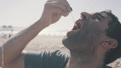 Young man taking tincture medicine with dropper at beach  photo