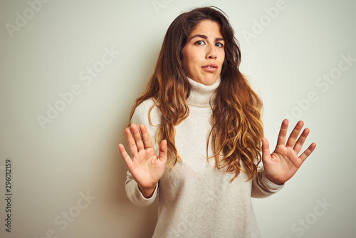 Young beautiful woman wearing winter sweater standing over white isolated background Moving away hands palms showing refusal and denial with afraid and disgusting expression. Stop and forbidden.