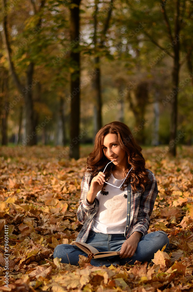 Beautiful girl with glasses sitting on the ground and reading book in park. Leisure time on warm autumn day. Autumn mood, enjoy the season Beautiful girl with glasses sitting on the ground and reading book in park. Leisure time on warm autumn day. Autumn mood, enjoy the season