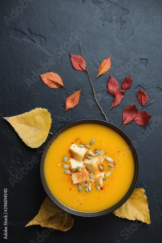 Bowl of pumpkin cream-soup over black stone background with autumn leaves, flatlay, studio shot