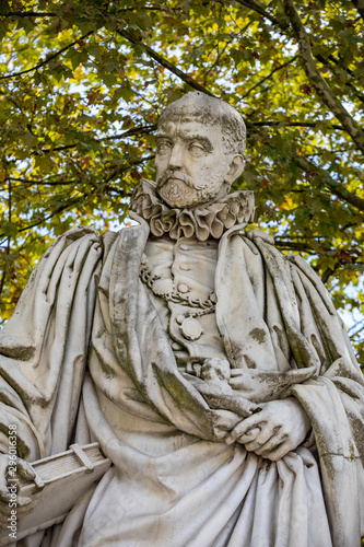 Statue of Michel de Montaigne in public garden along Place des Quinconces, Bordeaux France, with a canopy of green trees.