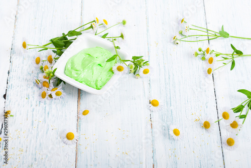 green cosmetis cream with chamomile flowers on white wooden table photo