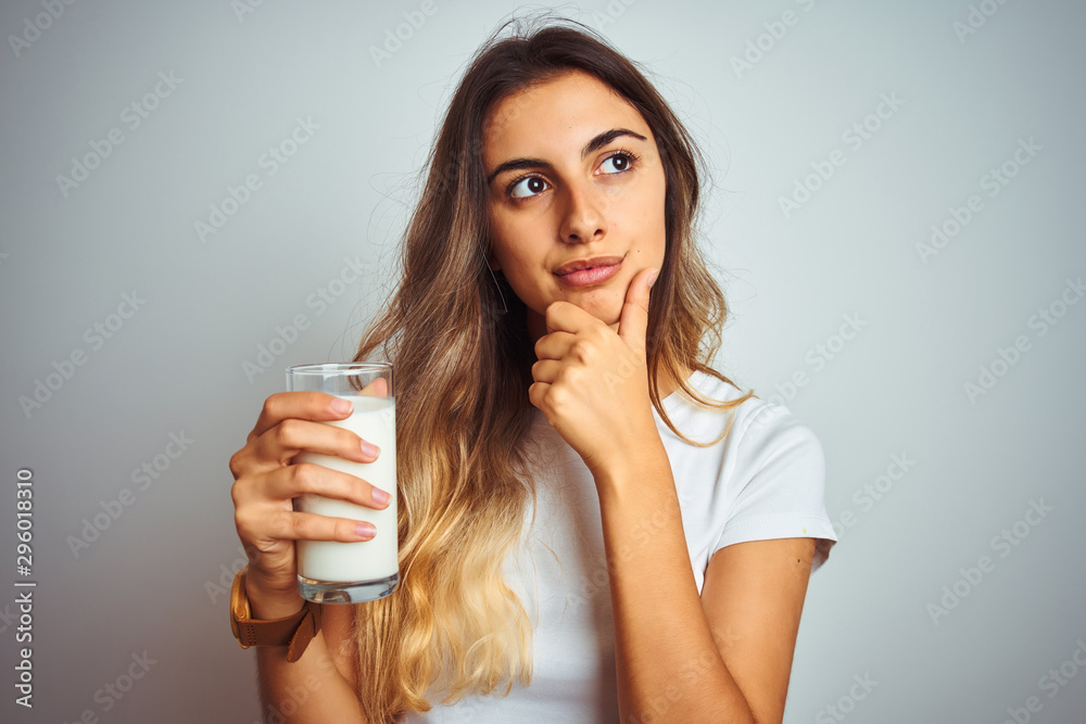 Young beautiful woman drinking a glass of milk over white isolated background serious face thinking about question, very confused idea Young beautiful woman drinking a glass of milk over white isolated background serious face thinking about question, very confused idea