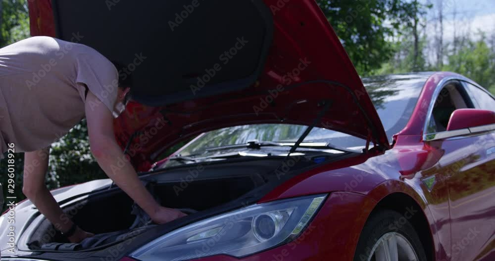 Young man grabing something from front trunk frunk of red electric sports car Young man grabing something from front trunk frunk of red electric sports car
