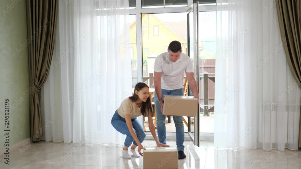 happy couple wearing jeans enters new house glass panoramic door holding big boxes and looking on nice interior happy couple wearing jeans enters new house glass panoramic door holding big boxes and looking on nice interior