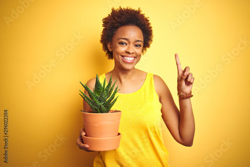 Young african american woman holding cactus pot over isolated yellow background surprised with an idea or question pointing finger with happy face, number one