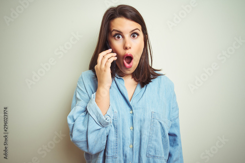 Young beautiful woman having a conversation using smartphone over isolated background scared in shock with a surprise face  afraid and excited with fear expression