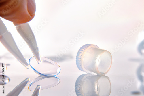 Hand with tweezers catching contact lenses on glass table