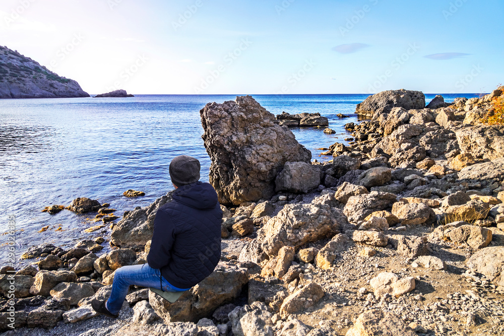 Tourist sits on a stone by the sea and looks into the distance. Crimea
