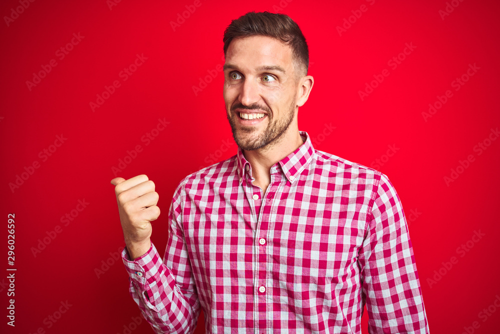 Young handsome man over red isolated background smiling with happy face looking and pointing to the side with thumb up. Young handsome man over red isolated background smiling with happy face looking and pointing to the side with thumb up.