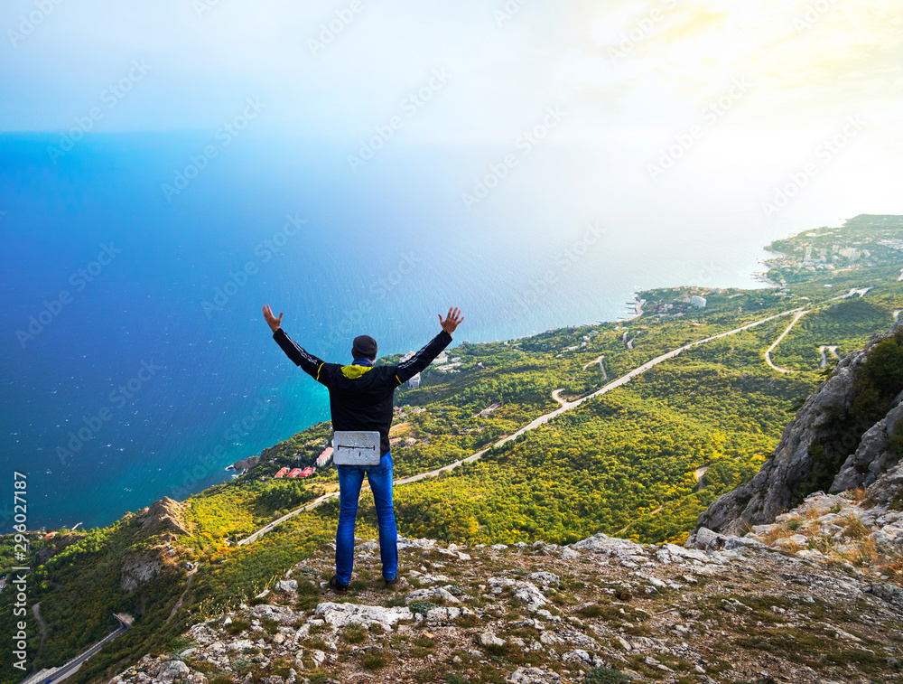 Man stands on the edge of a cliff with his arms raised up and looks at the sea. Crimea Man stands on the edge of a cliff with his arms raised up and looks at the sea. Crimea