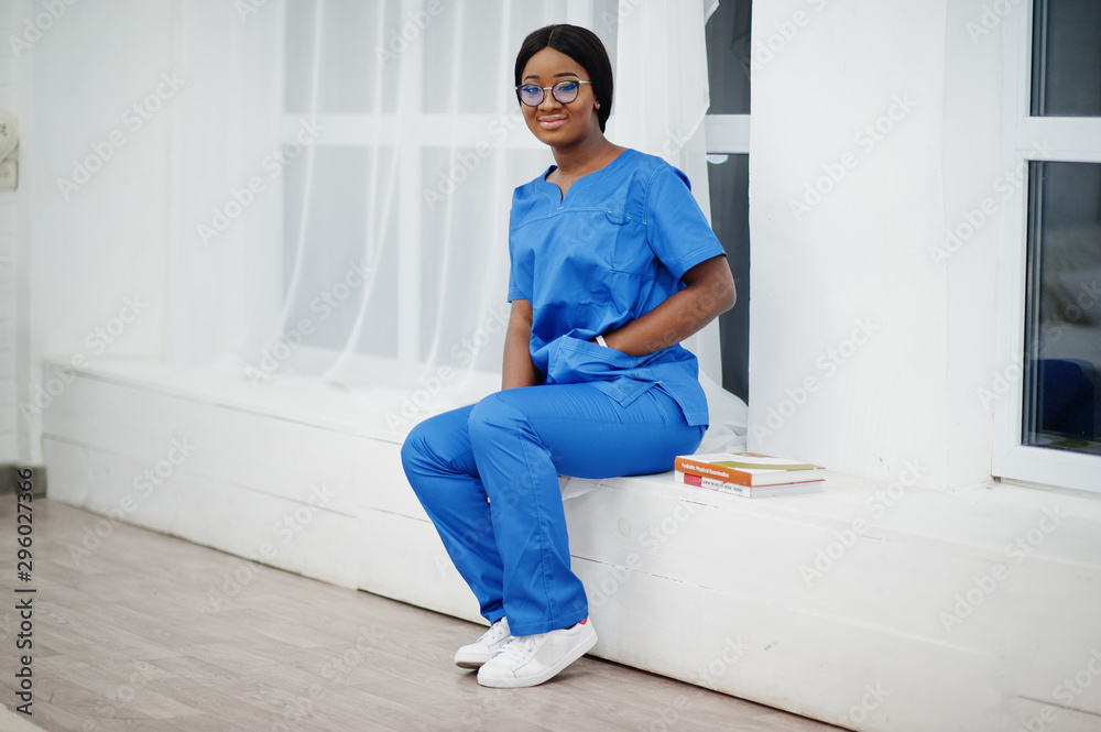 Portrait of happy female african american young doctor pediatrician in blue uniform coat and stethoscope with books at hands. Healthcare, medical, medicine specialist - concept. Portrait of happy female african american young doctor pediatrician in blue uniform coat and stethoscope with books at hands. Healthcare, medical, medicine specialist - concept.