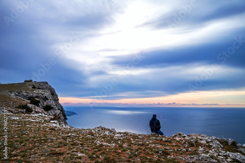 Tourist sits on a stone by the sea and looks into the distance. Crimea