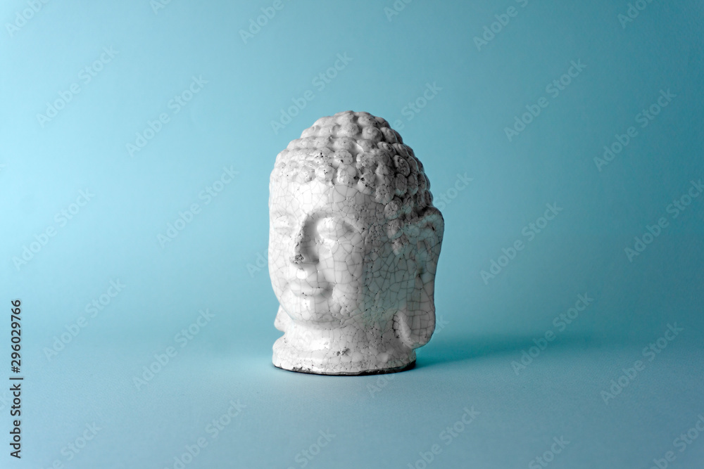 Ceramic head of a Buddha on a blue background. Minimal concept, copy space Ceramic head of a Buddha on a blue background. Minimal concept, copy space