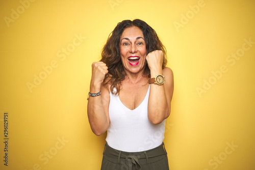 Middle age senior woman showing wrist watch over yellow isolated background screaming proud and celebrating victory and success very excited, cheering emotion
