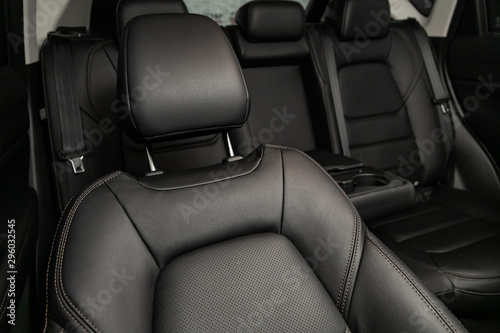 Close-up rear seat made of black leather with a head restraint, in the background passenger seats with seat belts. Luxury car interior