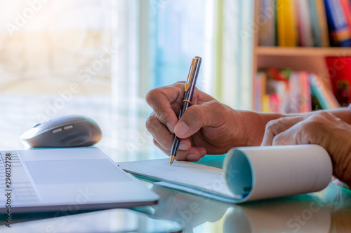 Business man hand writing and signing cheque book with laptop computer on the wooden table at modern home office.