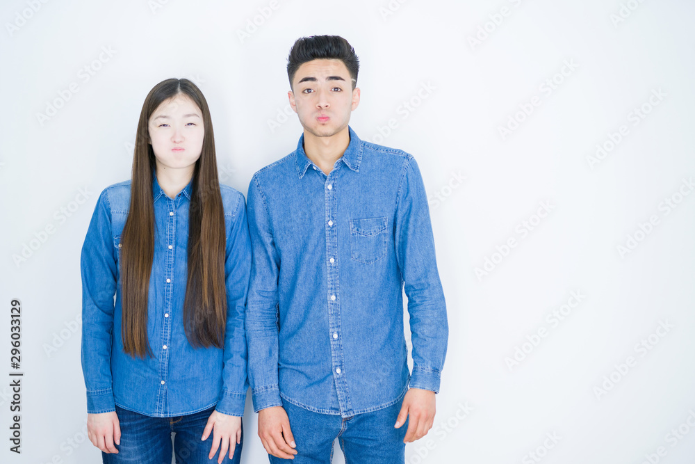 Beautiful young asian couple over white isolated background puffing cheeks with funny face. Mouth inflated with air, crazy expression.