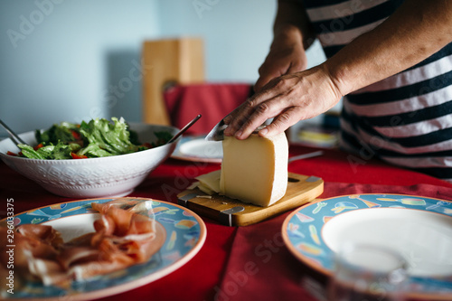 A dining table served with a bowl of salad, spanish jamon and a man slicing up a piece of cheese