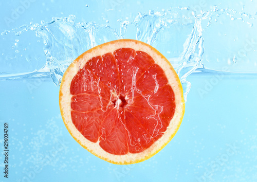 Fototapeta Naklejka Na Ścianę i Meble -  Falling of grapefruit piece into water on color background