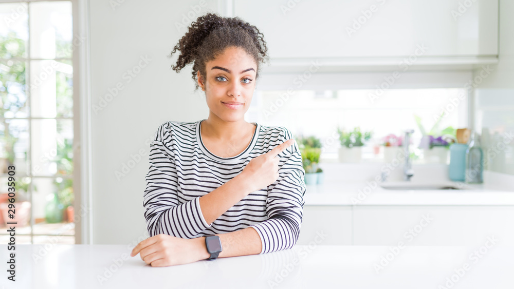 Beautiful african american woman with afro hair wearing casual striped sweater Pointing with hand finger to the side showing advertisement, serious and calm face Beautiful african american woman with afro hair wearing casual striped sweater Pointing with hand finger to the side showing advertisement, serious and calm face
