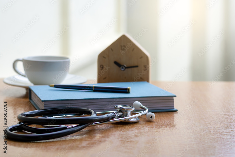 Mockup modern doctor's office desk with medical stethoscope, textbook, pen, alarm clock and white cup of coffee on wooden table. Medical education concept. Mockup modern doctor's office desk with medical stethoscope, textbook, pen, alarm clock and white cup of coffee on wooden table. Medical education concept.