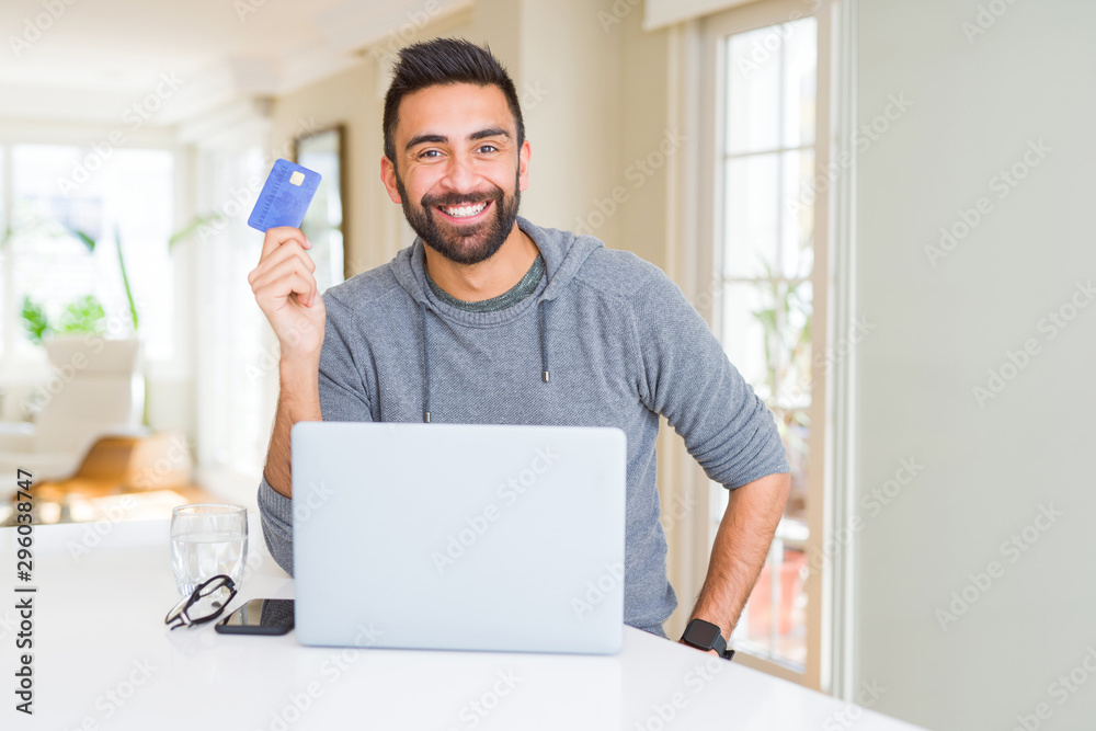 Handsome man smiling using credit card as payment metod when shopping online using laptop Handsome man smiling using credit card as payment metod when shopping online using laptop