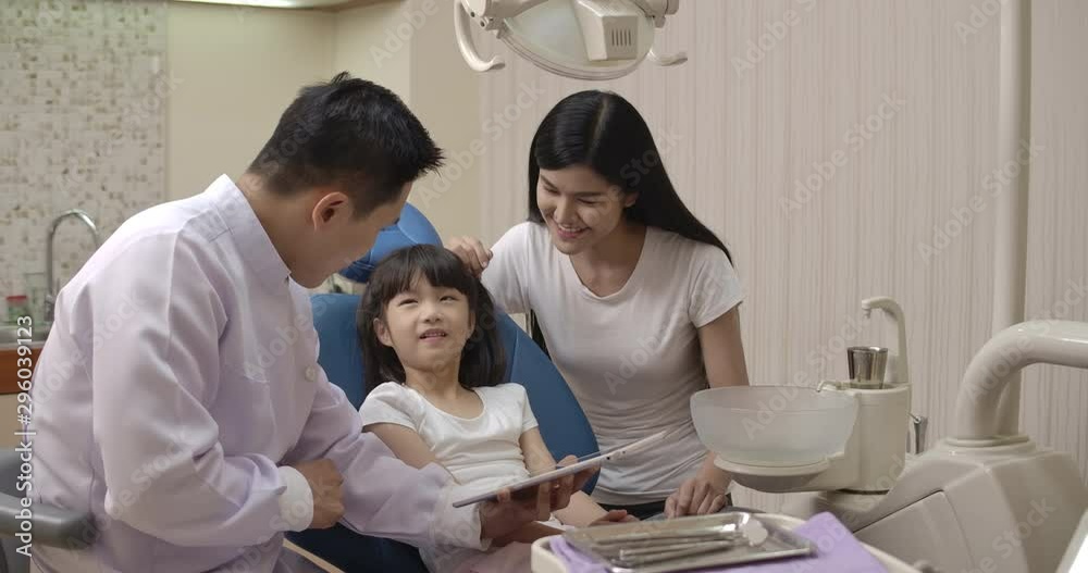 Dentist showing teeth x-ray image on digital tablet to patient. Dentist and patient choosing treatment in a consultation with medical equipment in the background. Dentist showing teeth x-ray image on digital tablet to patient. Dentist and patient choosing treatment in a consultation with medical equipment in the background.