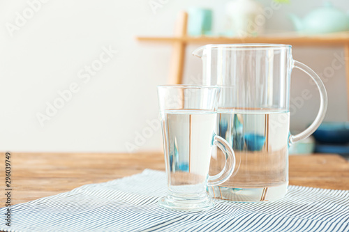 Glass cup and jug of fresh water on table indoors