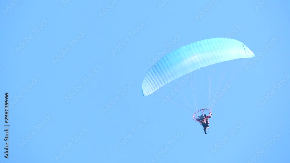 Parachute activity. Colorful paraglide wing flying with passenger in the blue cloudless sky, extreme sport, summer activities at the beach and in the mountain.