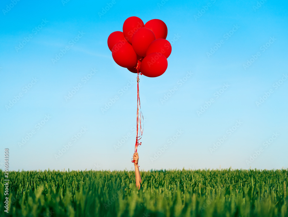 Hand holding red balloons in summer green field - obrazy, fototapety, plakaty 