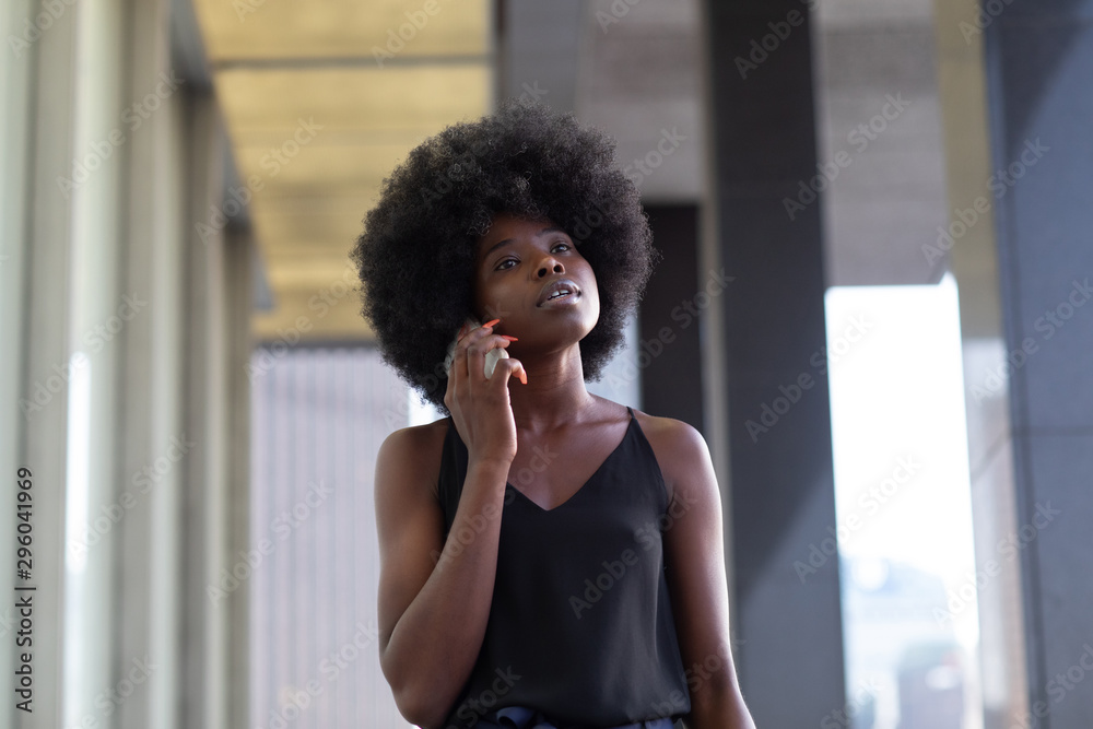 A pensive African american woman talking on a cell phone, city skyscrapers on the background A pensive African american woman talking on a cell phone, city skyscrapers on the background
