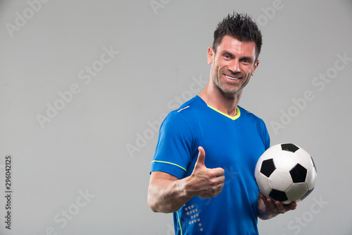 Happy soccer player holding ball isolated on a white background. Looking at camera