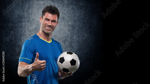 Happy soccer player holding ball isolated on a white background. Looking at camera