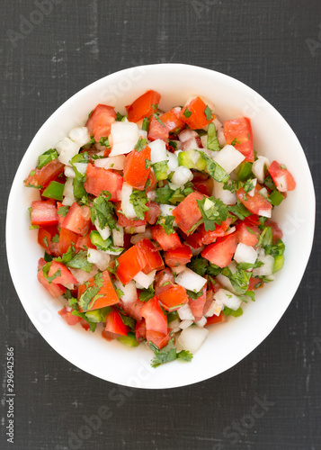 Pico de Gallo in a white bowl on a black surface. Overhead, from above, flat lay.