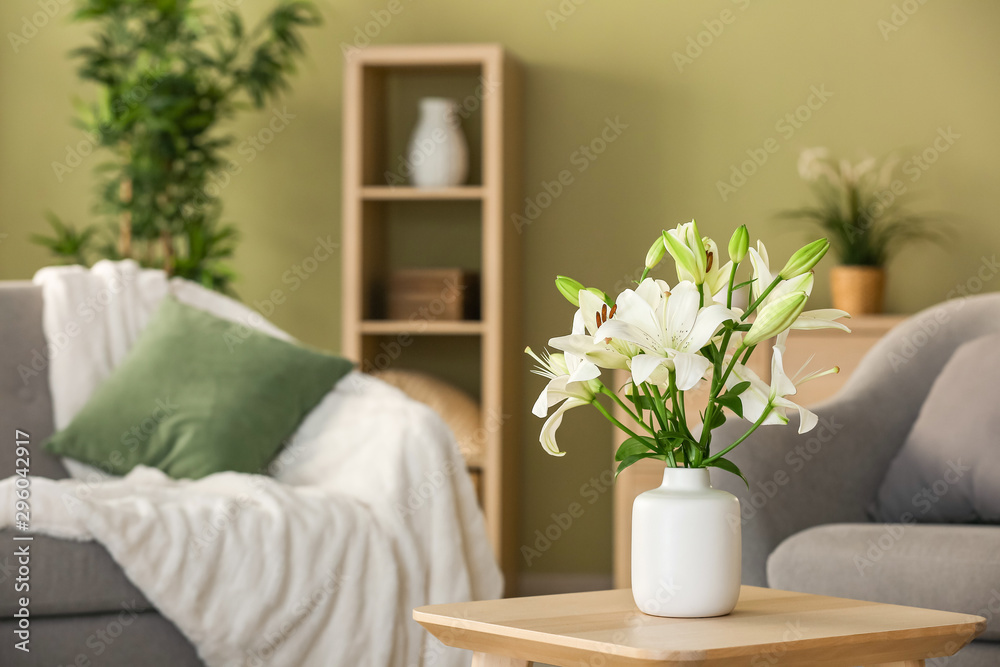 Naklejka premium Beautiful lily flowers in vase on table in room