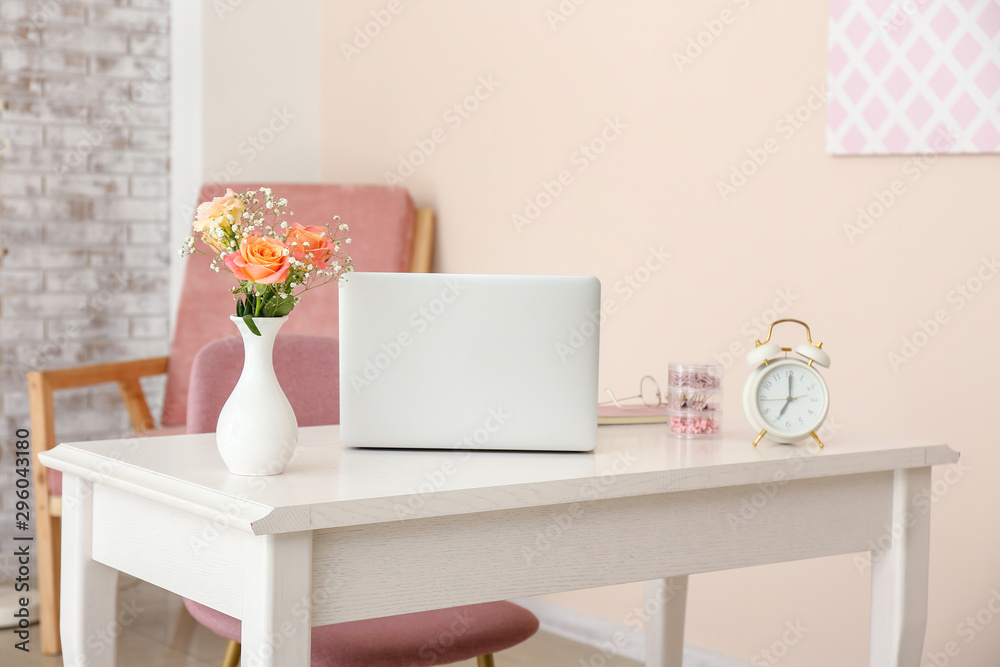 Fototapeta premium Beautiful bouquet in vase and laptop on table in room