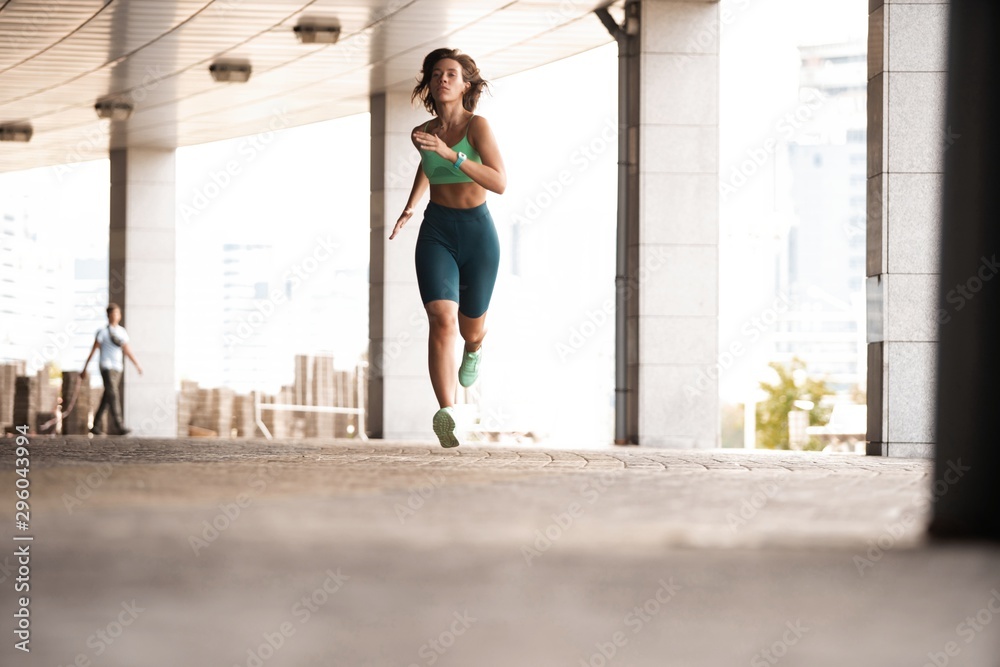 Sporty young woman athlete running on urban street in morning.