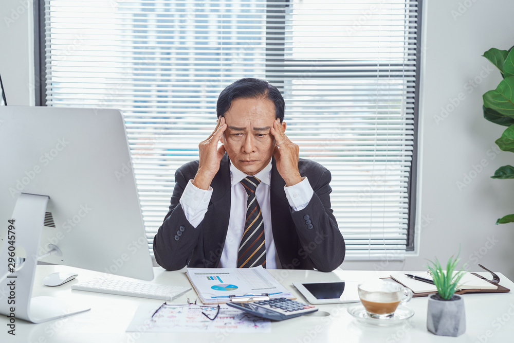 Middle aged Asian businessman feeling stressed and frustrated while working in work station. Business problem concept Middle aged Asian businessman feeling stressed and frustrated while working in work station. Business problem concept