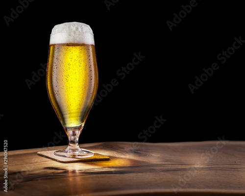 Glass of light beer on the bar counter on a black background.