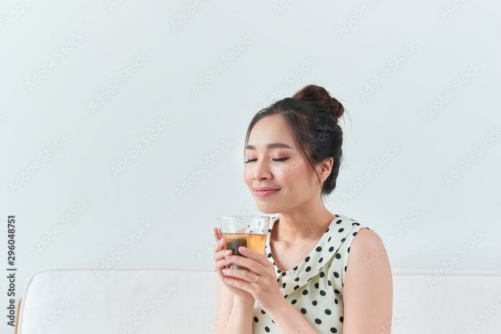 Happy asian woman sitting on her sofa holding cup at home Happy asian woman sitting on her sofa holding cup at home
