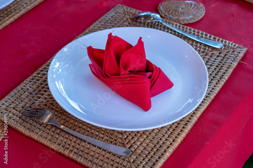 Elegant table setting with fork, spoon, white plate and red napkin in restaurant . Nice dining table set with arranged silverware and napkins