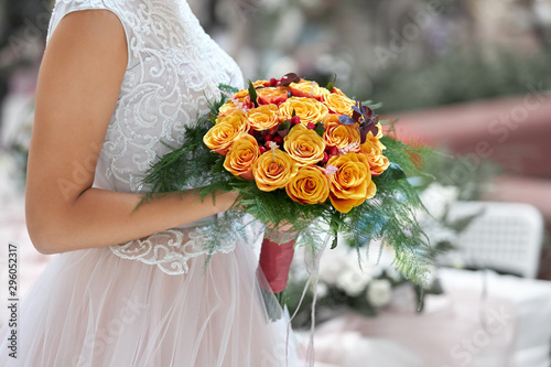 Bride in a beautiful white dress goes holding a wedding bouquet of orange roses in her hands.