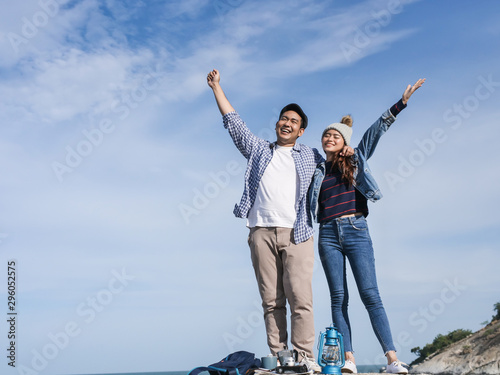 Happy Asian couple raising hands together with nature background, sunny day.