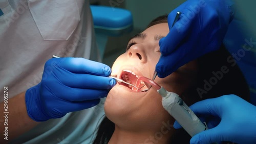 dentist in gloves sealing patient woman's teeth using dental mirror , dam and ejector during appointment in dental clinic