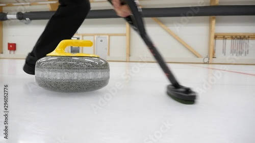 Curling game. Curler is sweeping the ice surface in the path of the stone. Curling granit stone is sliding and broom or brush is sweeping. Concept: winter games, winter olympic sports.