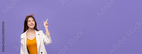 Asian girl pointing hand to empty space on purple banner background