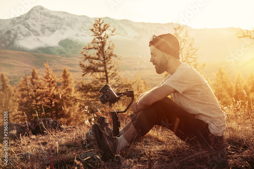 Man sits with gimbal and camera against mountains photo