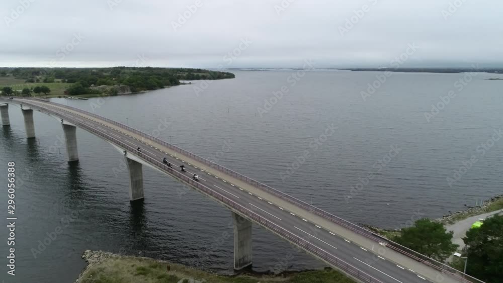 Aerial view of Scandinavian landscape and bridge. Group of motorcyclist riding through the long modern bridge. Sweden, Oland region. Typical Swedish weather. Aerial view of Scandinavian landscape and bridge. Group of motorcyclist riding through the long modern bridge. Sweden, Oland region. Typical Swedish weather.